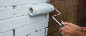 a person painting an exterior brick wall